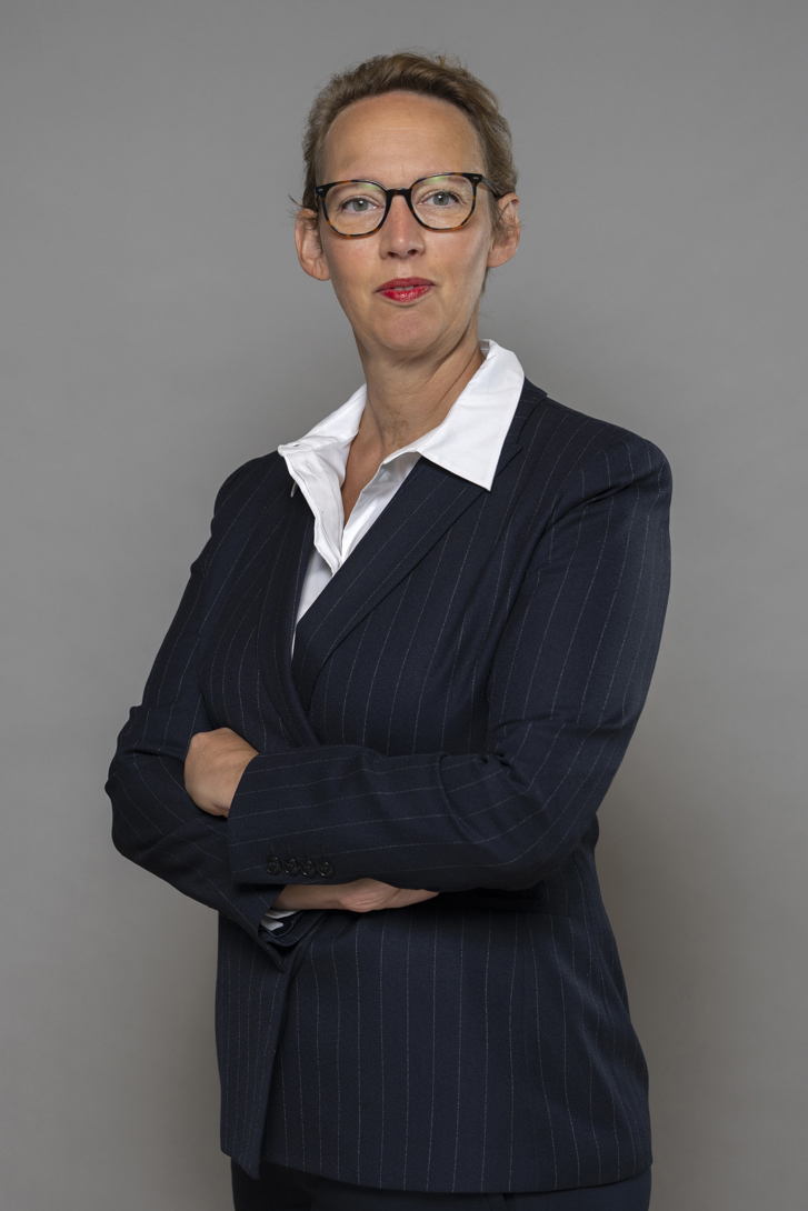 Bild föreställande ambassadör Catharina Cappelin. Ambassadör Cappelin står upp med armarna i kors och är klädd i kritstrecksrandig dräkt och en vit skjorta. Hon har kort blont hår och bär runda mörka glasögon.